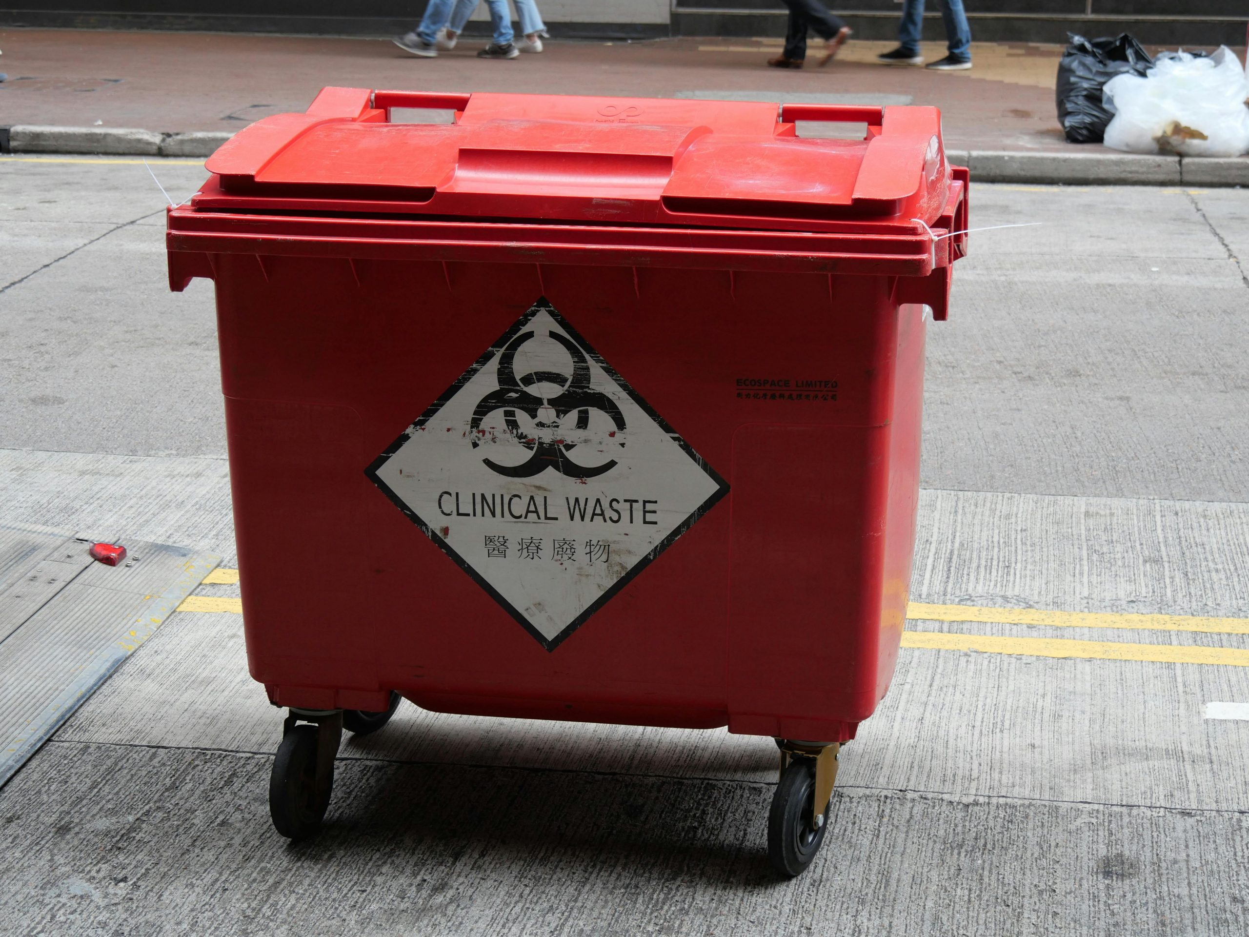 A red wheeled bin labeled for clinical waste management on a city street.